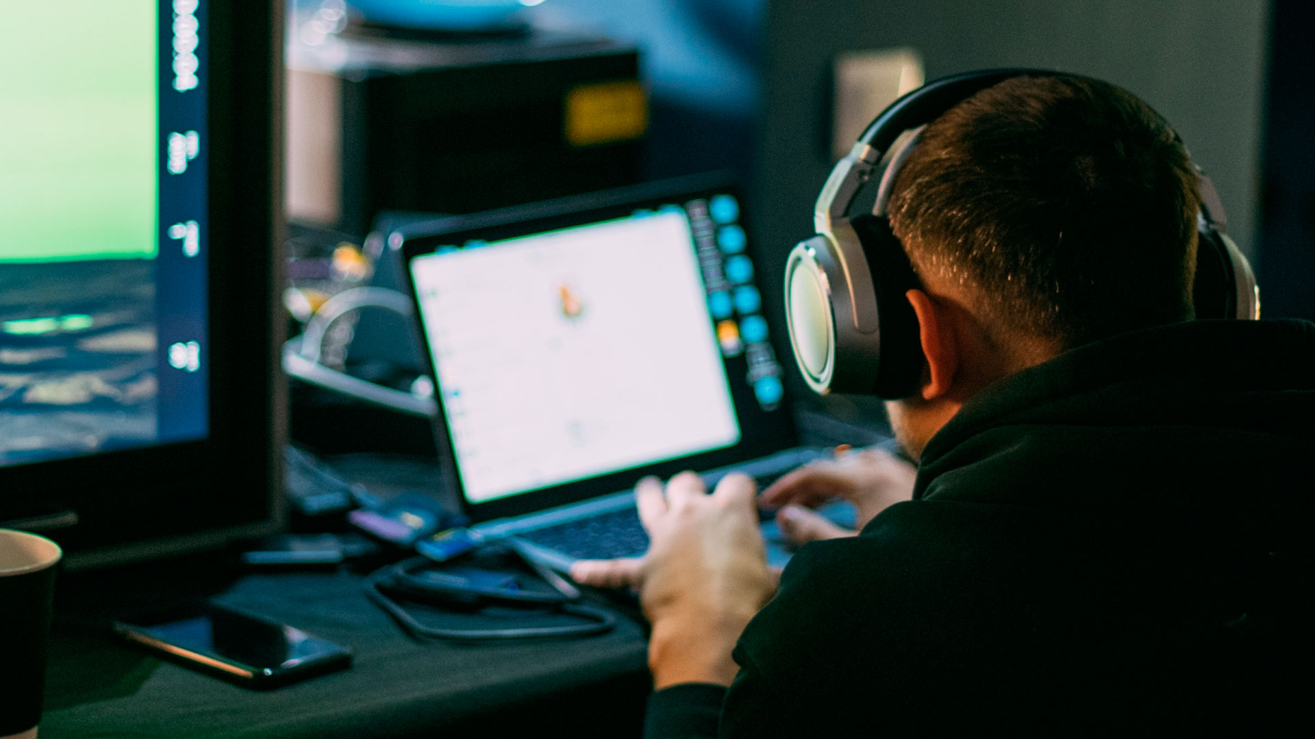 man hunches over a workstation with headphones on