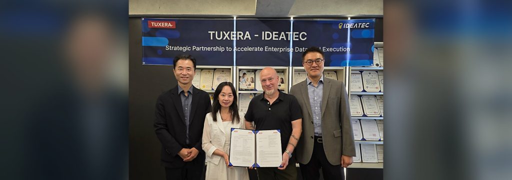 Four executives stand holding the signed Tuxera–IDEATEC agreement beneath a banner reading "Tuxera – IDEATEC: Strategic Partnership to Accelerate Enterprise Data and AI Execution.